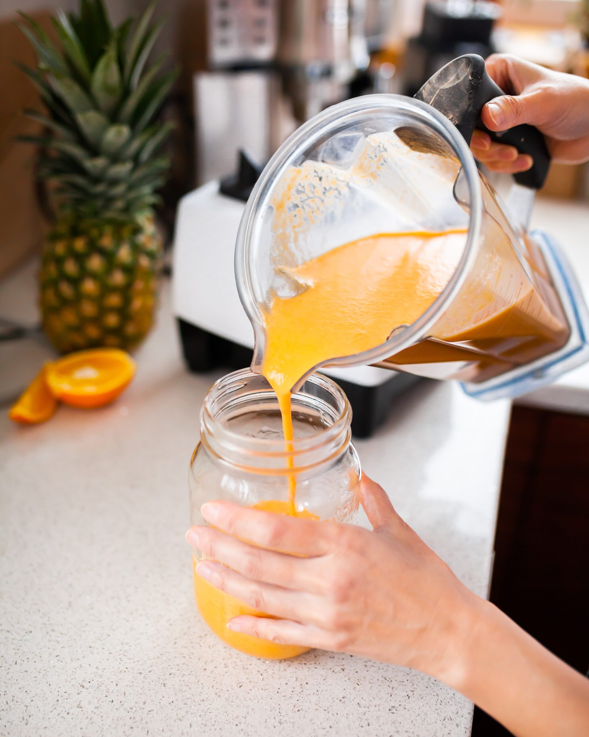 A yellow smoothie is being poured from a blender into a mason jar