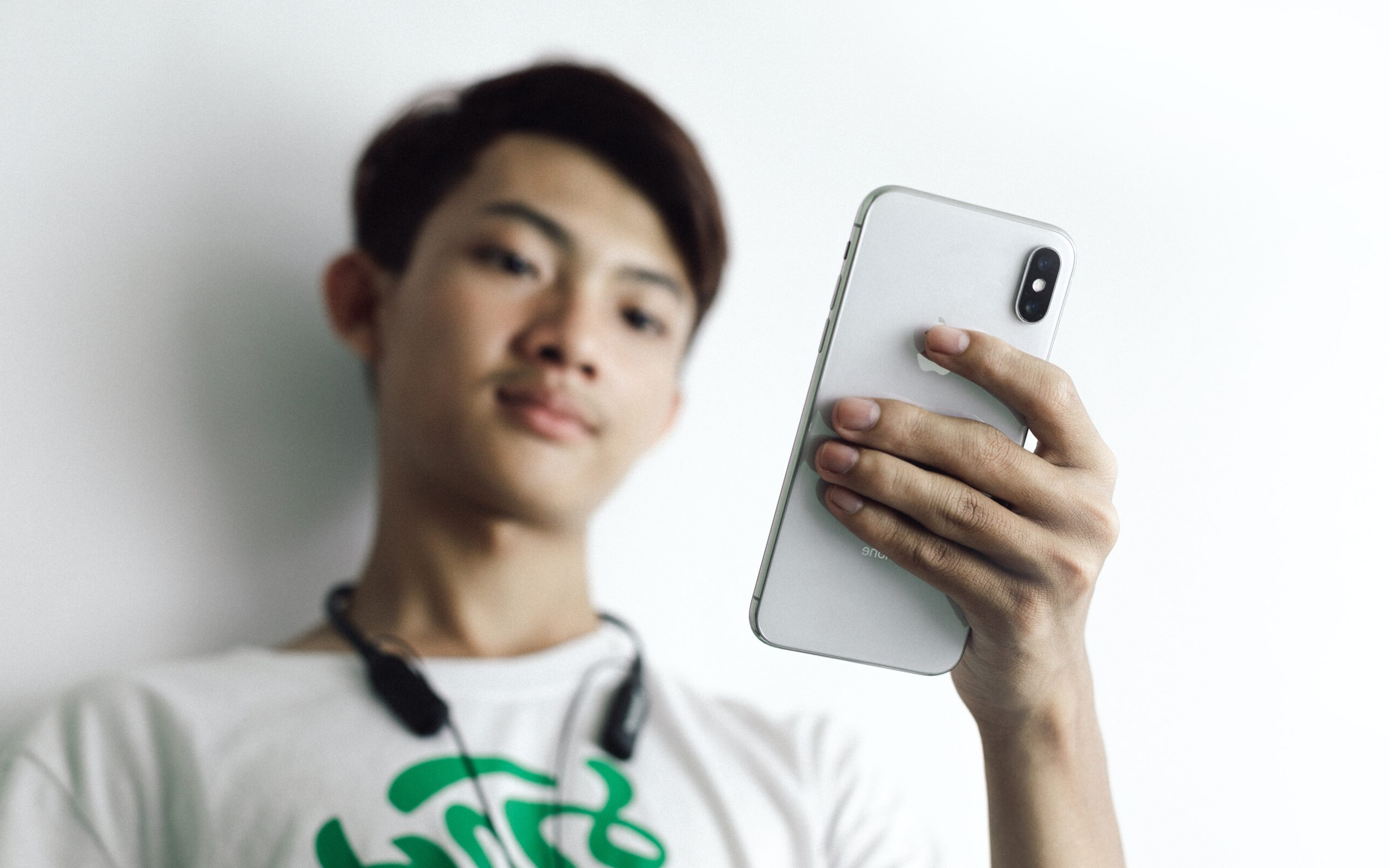 Asian male wearing headphones around his neck typing into a white iphone