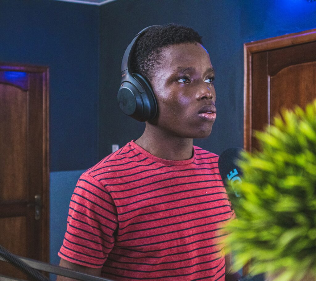 A young Black male wearing headphones, standing and looking intently at a computer screen, using binaural beats to enhance focus and concentration. The image illustrates how sound therapy can help improve mental clarity and productivity, featured in a blog post on the Invigorate Your Journey Blog.