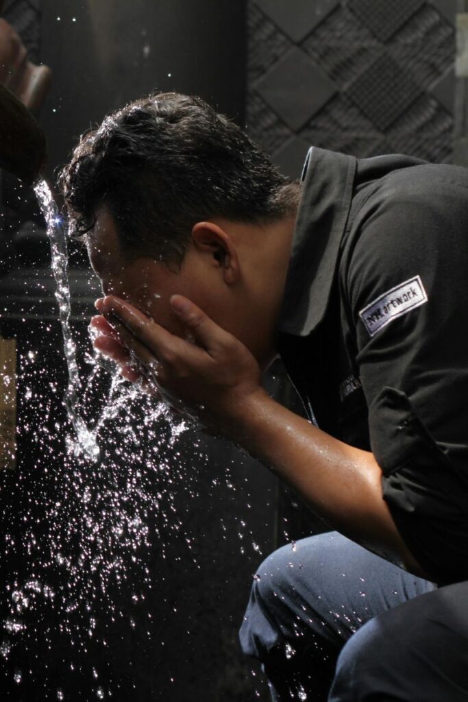 Man splashing water on his face at work to boost circulation and increase alertness, a simple energy-boosting strategy to overcome fatigue.