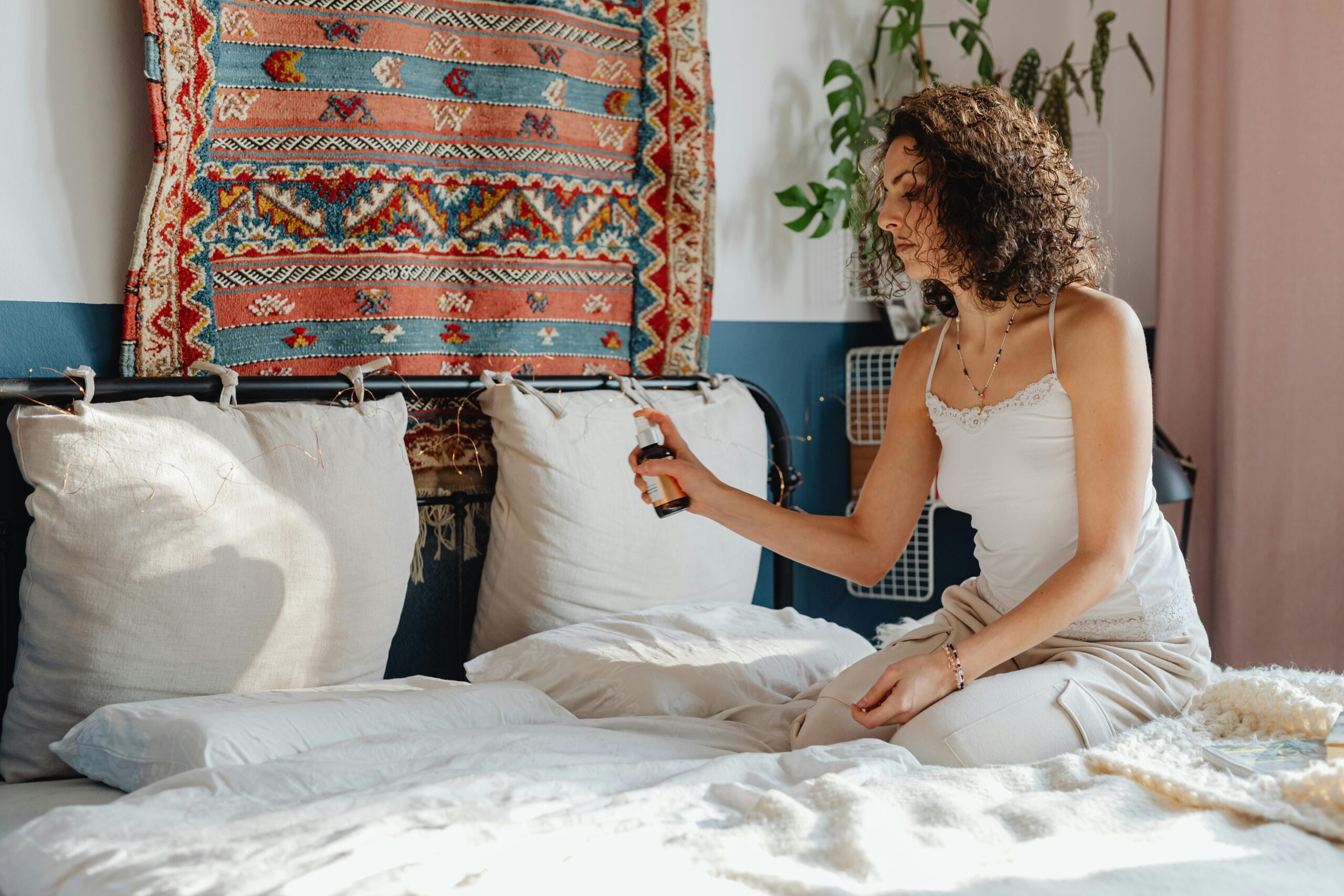 A woman sprays a calming sleep-promoting mist on her pillow, enhancing her bedtime routine to support health, wellness, and restful sleep. This practice can be especially beneficial for individuals managing autoimmune diseases or chronic illness, promoting relaxation and better sleep quality.