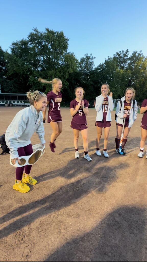 A group of enthusiastic female athletes celebrating together on a dirt field, showcasing joy and camaraderie after a game.